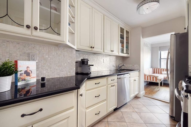 kitchen featuring dark countertops, glass insert cabinets, tasteful backsplash, appliances with stainless steel finishes, and light tile patterned floors
