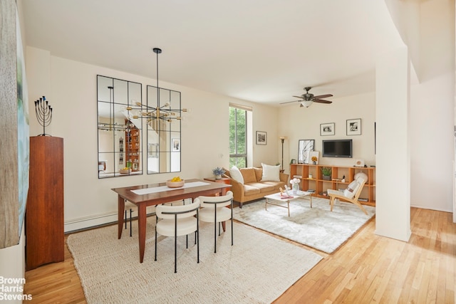 dining area with a baseboard heating unit, ceiling fan with notable chandelier, and wood finished floors