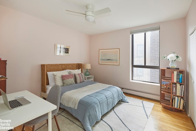 bedroom with light wood-style floors, baseboard heating, and a ceiling fan