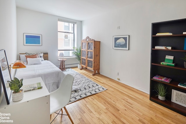 bedroom with a baseboard radiator, baseboards, and hardwood / wood-style floors