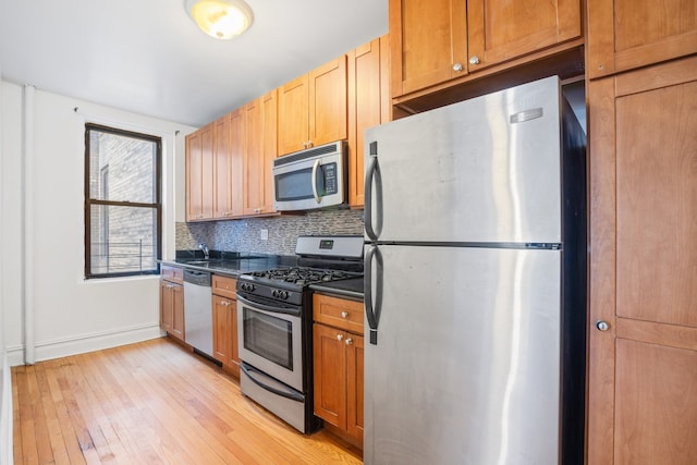 kitchen featuring dark countertops, light wood-style flooring, backsplash, appliances with stainless steel finishes, and baseboards