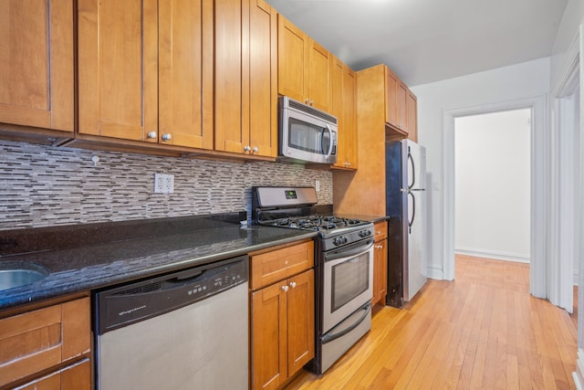 kitchen featuring light wood-style flooring, appliances with stainless steel finishes, decorative backsplash, and dark stone counters