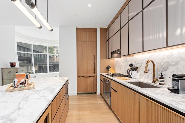 kitchen featuring light wood-style floors, a sink, decorative backsplash, and light stone countertops