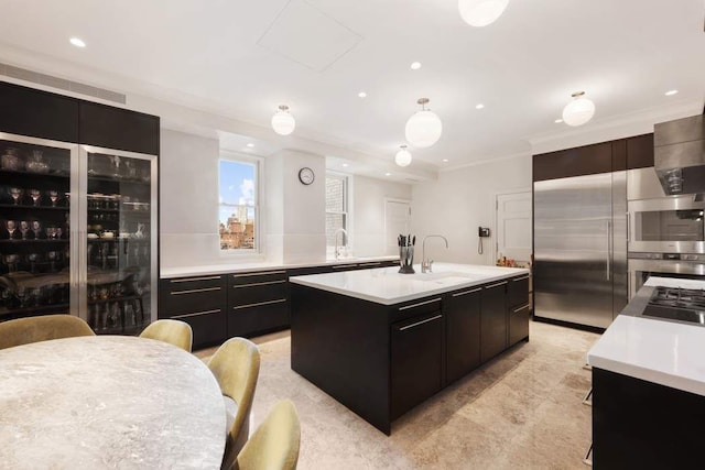 kitchen featuring an island with sink, light countertops, recessed lighting, a sink, and dark cabinetry