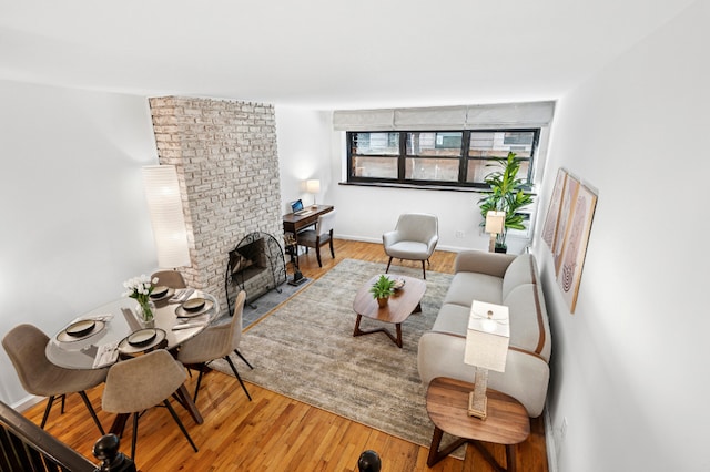 living area with a brick fireplace, baseboards, and wood finished floors