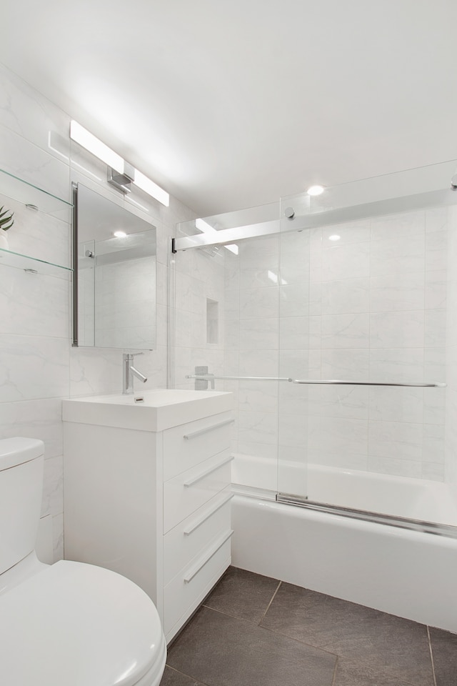 full bath featuring tile walls, toilet, vanity, and shower / bath combination with glass door