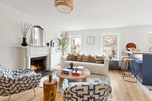 living room with radiator heating unit, light wood-type flooring, and a fireplace with flush hearth