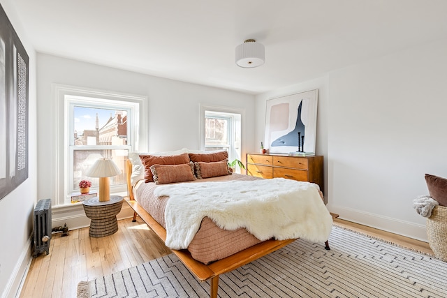 bedroom featuring light wood finished floors, radiator heating unit, and baseboards