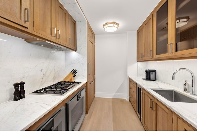 kitchen featuring brown cabinets, a sink, wall oven, light stone countertops, and stainless steel gas cooktop