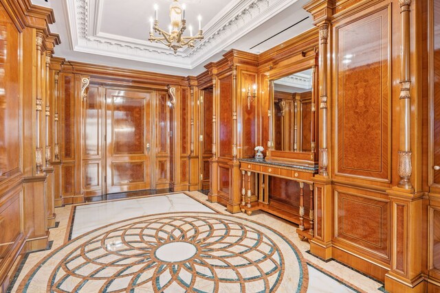 foyer entrance with a tray ceiling, marble finish floor, a notable chandelier, a decorative wall, and ornamental molding