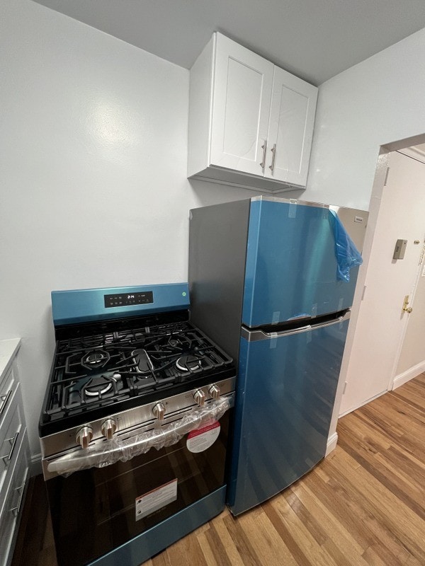 kitchen with white cabinetry, stainless steel appliances, light wood-type flooring, and baseboards