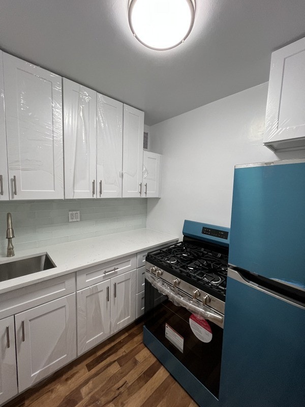 kitchen featuring a sink, backsplash, dark wood-style floors, freestanding refrigerator, and gas range