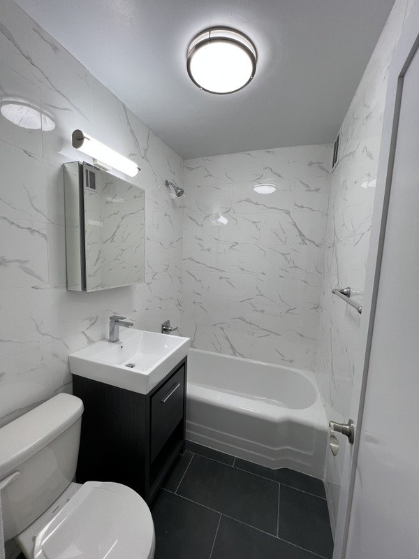 bathroom featuring tile patterned floors, toilet, tile walls, bathtub / shower combination, and vanity