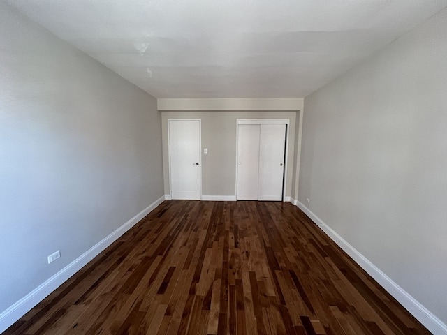 unfurnished bedroom with dark wood-style floors, a closet, and baseboards