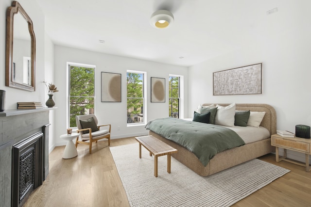 bedroom featuring multiple windows, a fireplace, light wood-type flooring, and baseboards