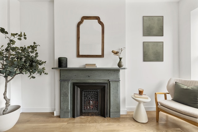 sitting room with wood finished floors, baseboards, and a lit fireplace