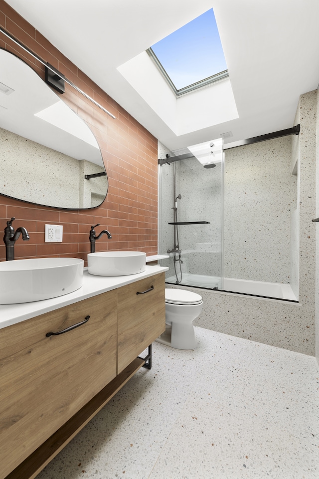 bathroom with double vanity, combined bath / shower with glass door, toilet, and a sink