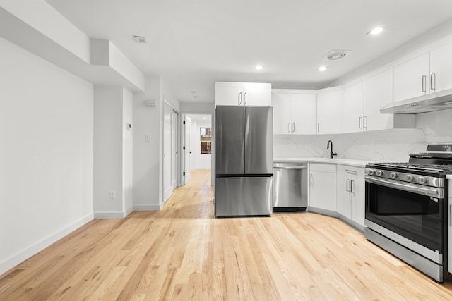 kitchen with under cabinet range hood, a sink, backsplash, appliances with stainless steel finishes, and light countertops