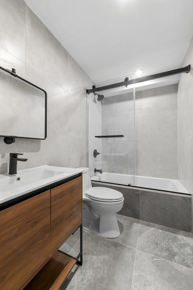 bathroom featuring vanity, toilet, tile walls, and bath / shower combo with glass door