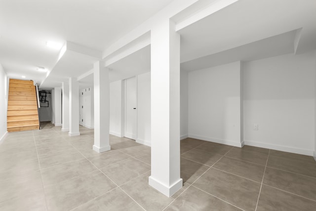 finished below grade area with stairway, light tile patterned floors, and baseboards