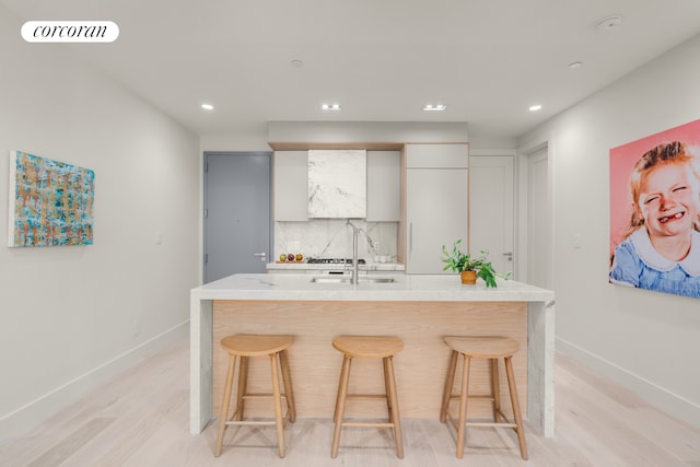 kitchen featuring baseboards, visible vents, decorative backsplash, a kitchen breakfast bar, and light countertops