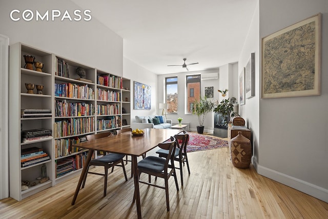 dining room featuring baseboards, hardwood / wood-style floors, a ceiling fan, and a wall unit AC