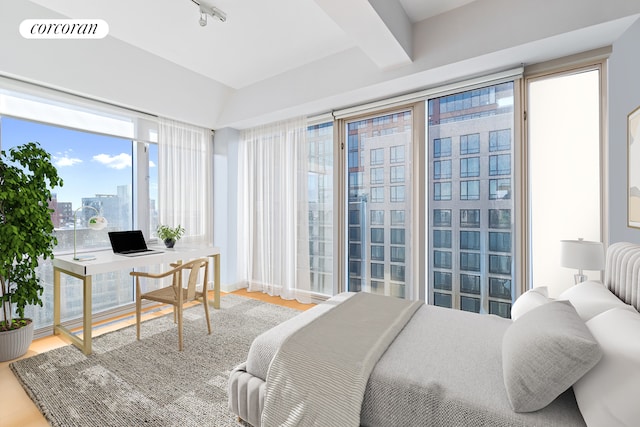 bedroom with vaulted ceiling with beams, a city view, wood finished floors, visible vents, and rail lighting