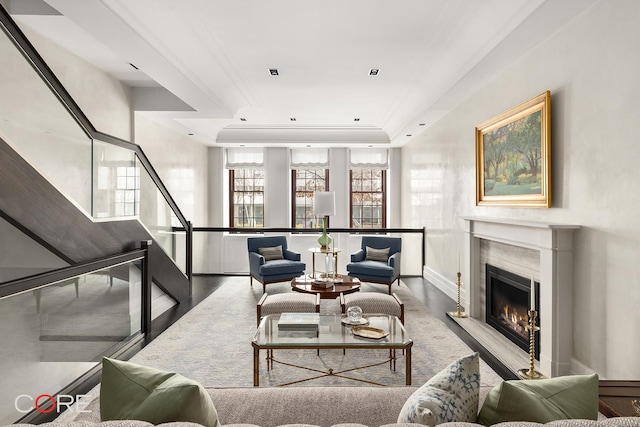 living area featuring wood finished floors, a warm lit fireplace, a raised ceiling, and crown molding