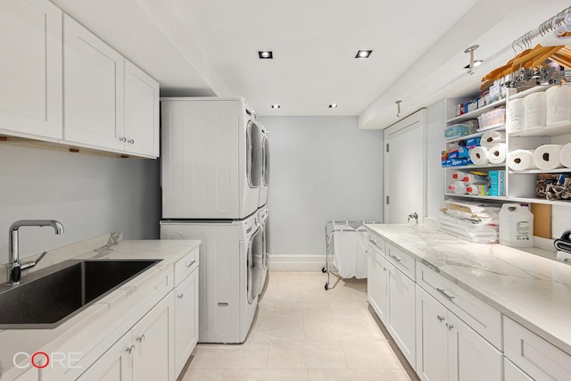 washroom with light tile patterned floors, cabinet space, stacked washer / dryer, a sink, and baseboards