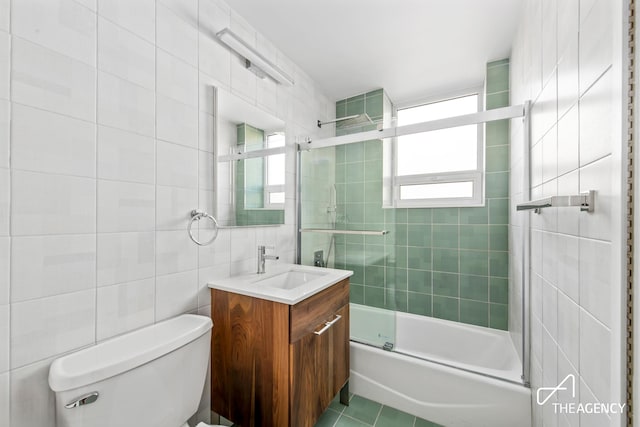 full bathroom featuring toilet, tile walls, tile patterned flooring, bath / shower combo with glass door, and vanity