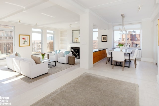 living area featuring built in features, crown molding, a fireplace, and a notable chandelier