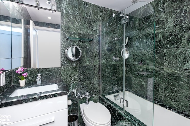 bathroom featuring combined bath / shower with glass door, toilet, tile walls, and vanity