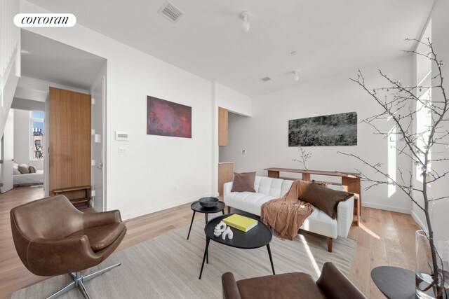 living area with light wood finished floors, visible vents, and baseboards