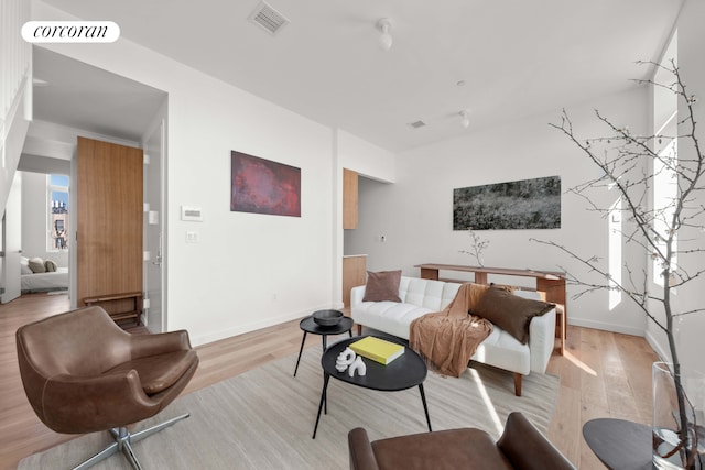 living area featuring light wood-style floors, visible vents, and baseboards