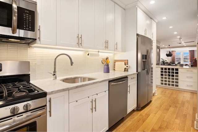 kitchen featuring appliances with stainless steel finishes, light stone countertops, light wood-style floors, white cabinetry, and a sink