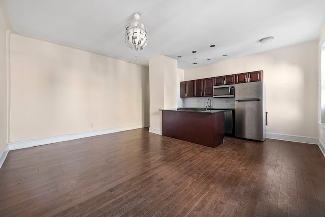 kitchen featuring dark countertops, dark brown cabinets, open floor plan, appliances with stainless steel finishes, and dark wood-style flooring