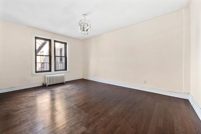 unfurnished room featuring dark wood-style floors, a notable chandelier, radiator, and baseboards