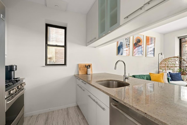 kitchen featuring light stone counters, stainless steel appliances, a sink, white cabinetry, and glass insert cabinets