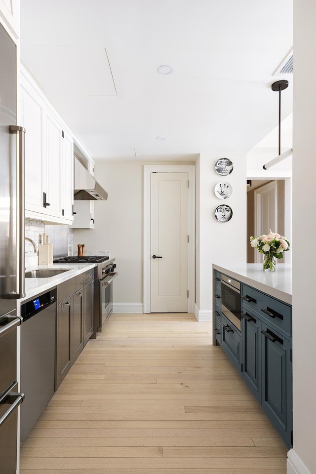 kitchen featuring light wood-style flooring, appliances with stainless steel finishes, under cabinet range hood, white cabinetry, and a sink