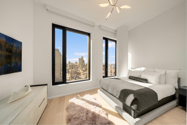 bedroom with a city view, light wood-style flooring, and baseboards