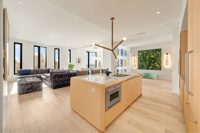 kitchen with open floor plan, light wood finished floors, a sink, and stainless steel oven