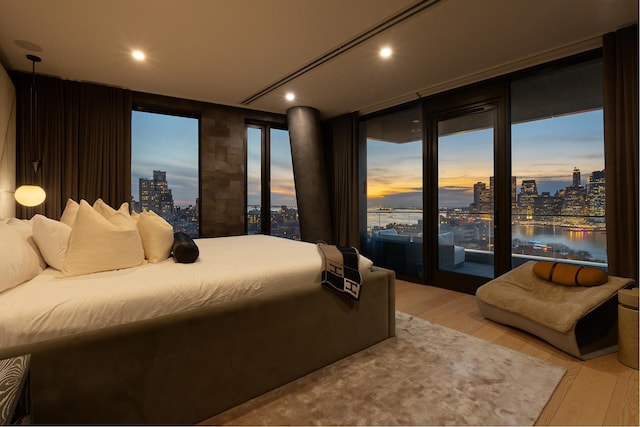 bedroom featuring light wood-type flooring, a water view, a view of city, and recessed lighting