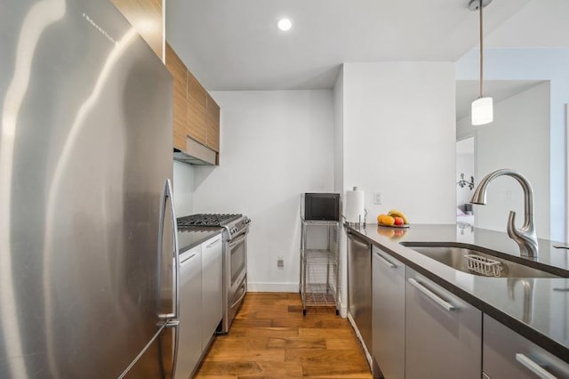 kitchen featuring dark countertops, modern cabinets, wood finished floors, stainless steel appliances, and a sink