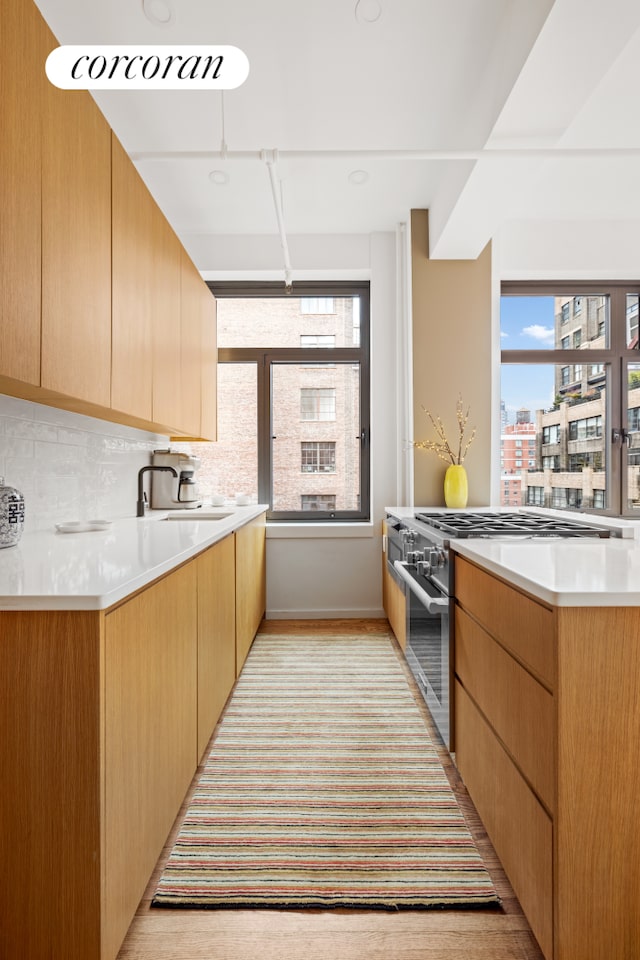 kitchen featuring light brown cabinets, a sink, light countertops, high end range, and decorative backsplash