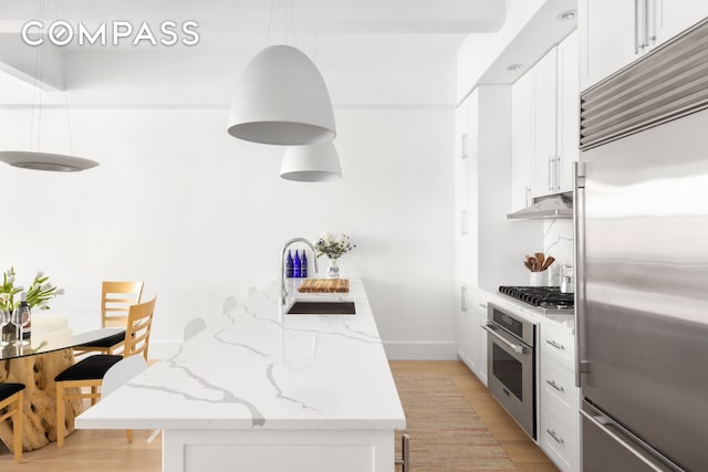 kitchen featuring light stone countertops, light wood-style flooring, appliances with stainless steel finishes, white cabinetry, and a sink