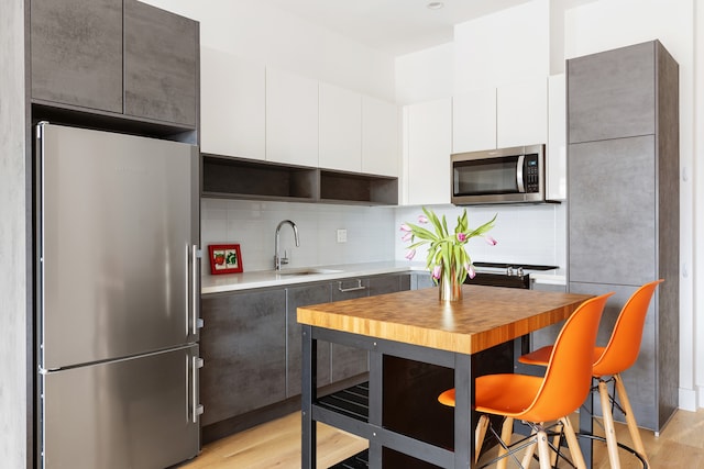 kitchen featuring stainless steel appliances, white cabinetry, light countertops, decorative backsplash, and light wood finished floors