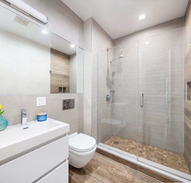 bathroom with toilet, wood finished floors, vanity, tile walls, and a shower stall