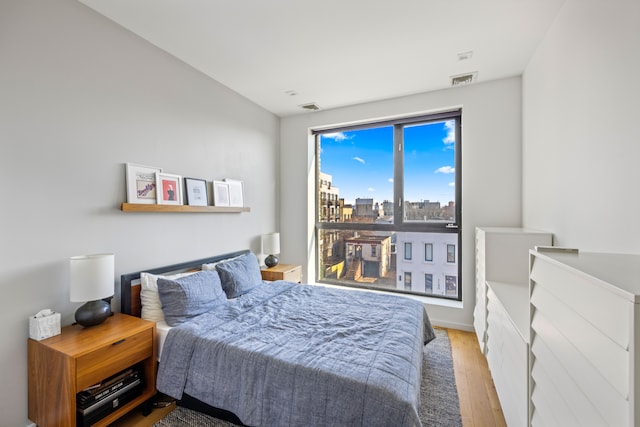 bedroom with a view of city, visible vents, and wood finished floors