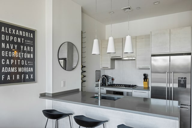 kitchen featuring high end refrigerator, a sink, visible vents, gas stovetop, and a kitchen breakfast bar