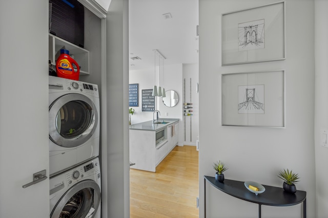 clothes washing area featuring laundry area, stacked washer / dryer, a sink, and light wood-style floors